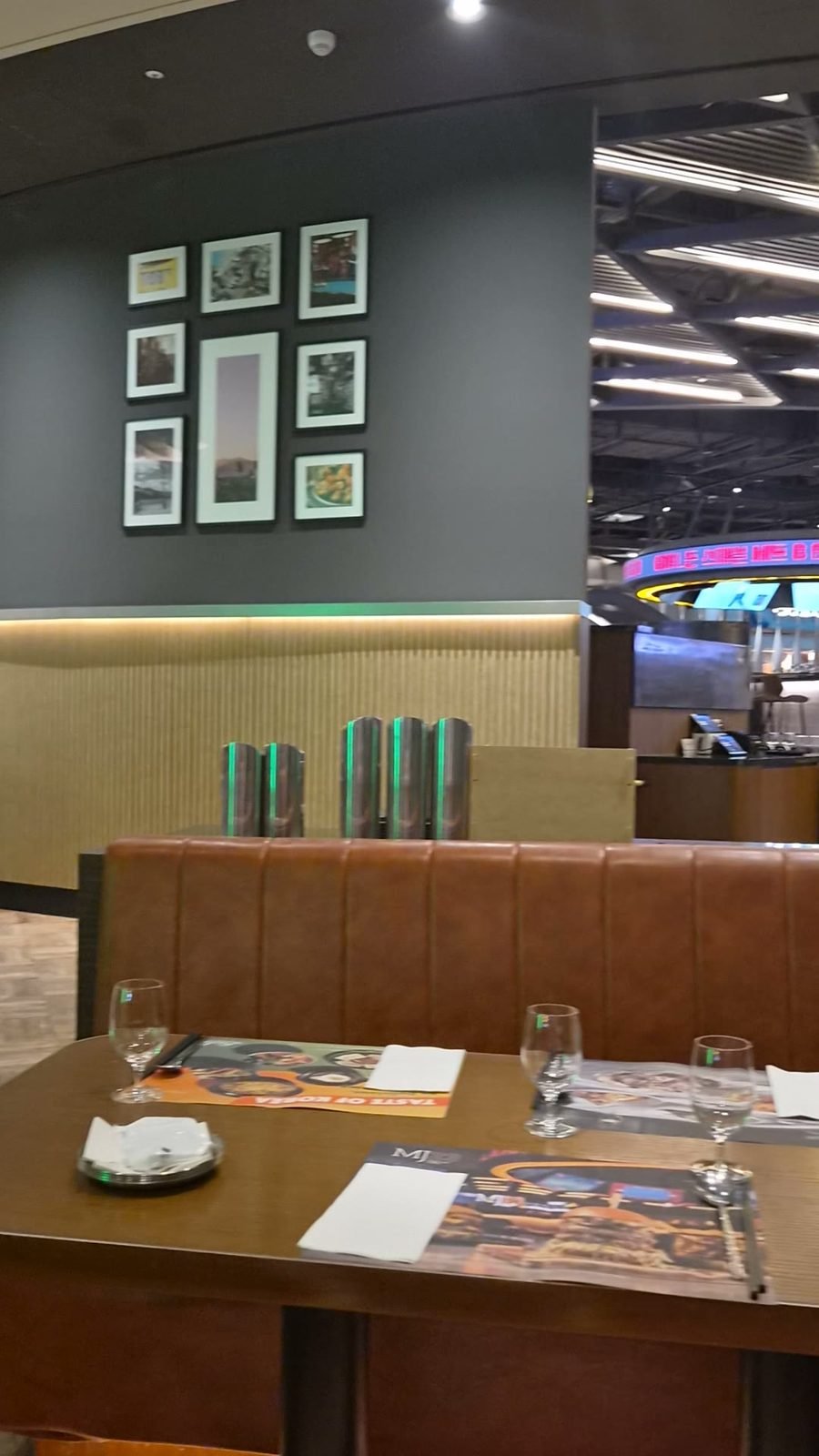 Booth seating at MJ23 with a set table, framed pictures on a dark wall and a row of glasses on a side counter.