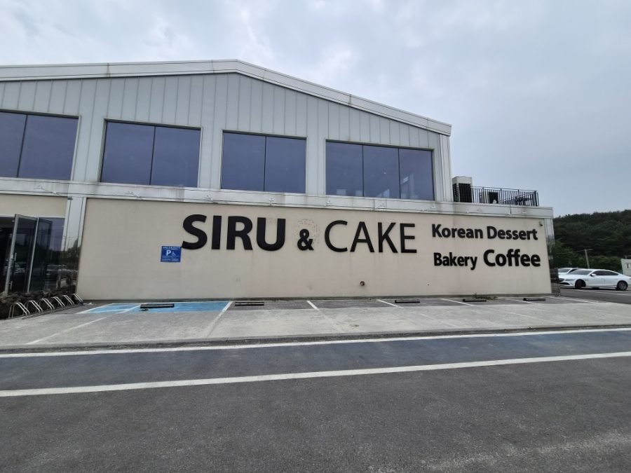 The cafe's concrete exterior with SIRU & CAKE painted on the wall above the words Korean Dessert, Bakery, Coffee.