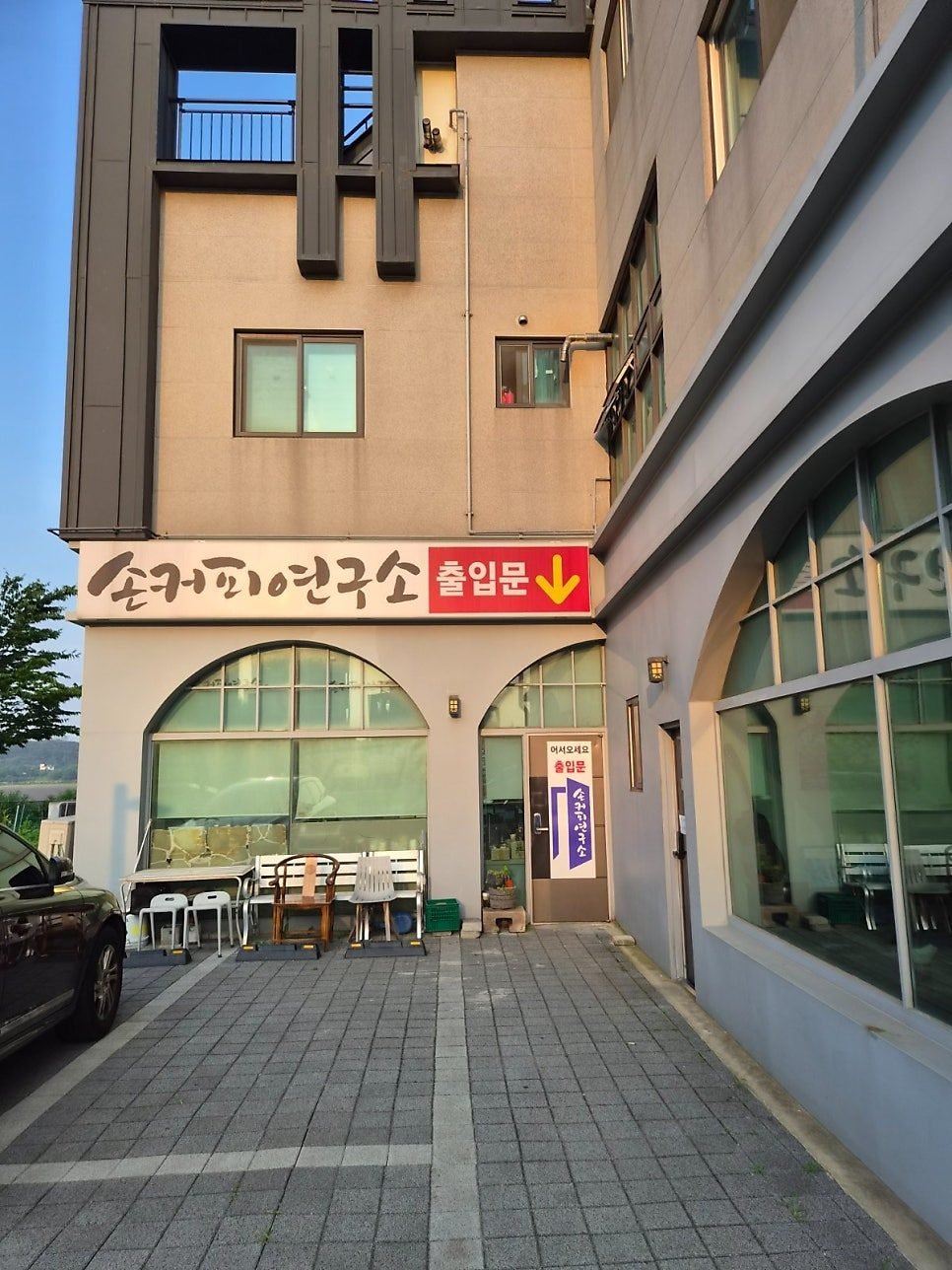White shop sign reading 손커피연구소 above arched windows, with a red panel and a yellow arrow pointing down at the entrance door