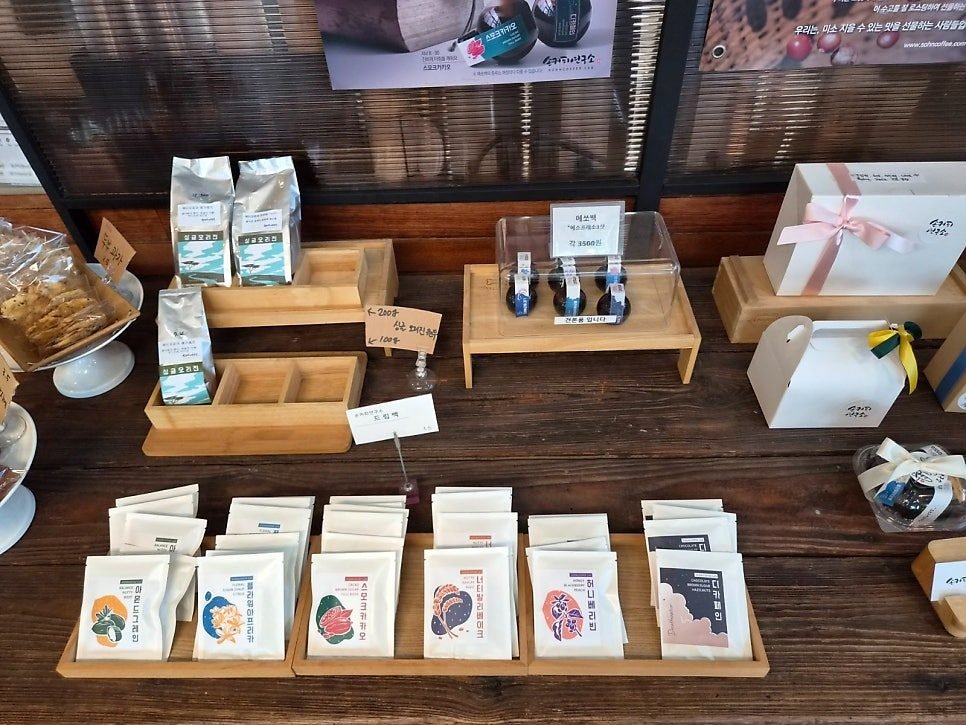 Wooden retail counter with six kinds of drip bag packets in trays, bags of single origin beans, small espresso packs under a cover and ribboned gift boxes