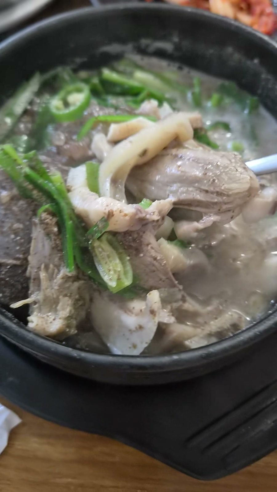 Sliced head meat and blood sausage lifted out of a milky broth in a black stone bowl, topped with green onion