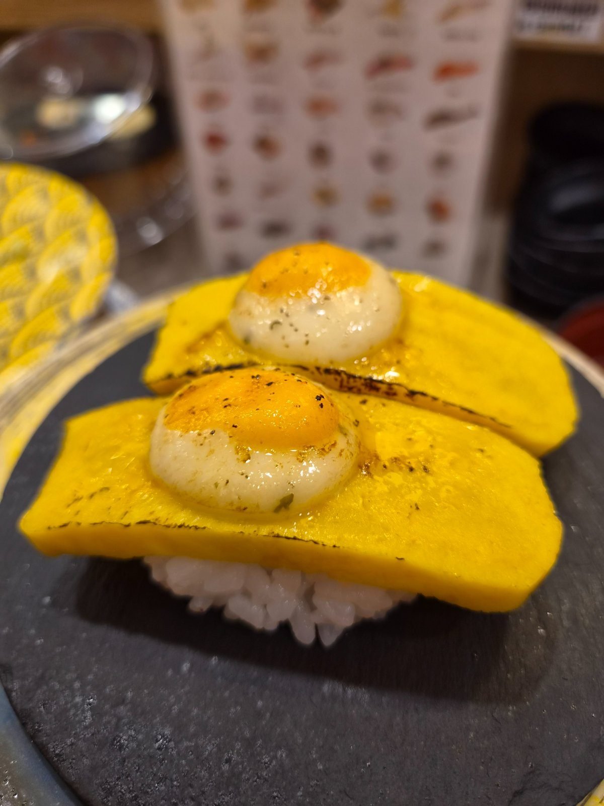 Two pieces of egg sushi with a round slice of melted cheese torched on top