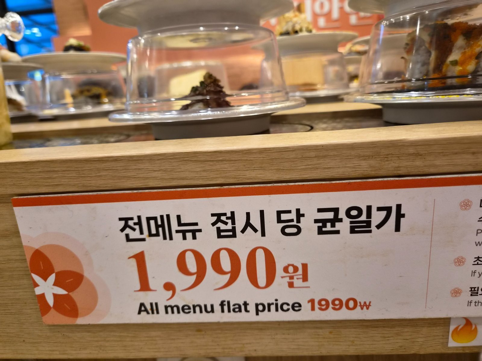 Sign on the conveyor belt rail reading 전메뉴 접시 당 균일가 1,990원 and All menu flat price 1990W