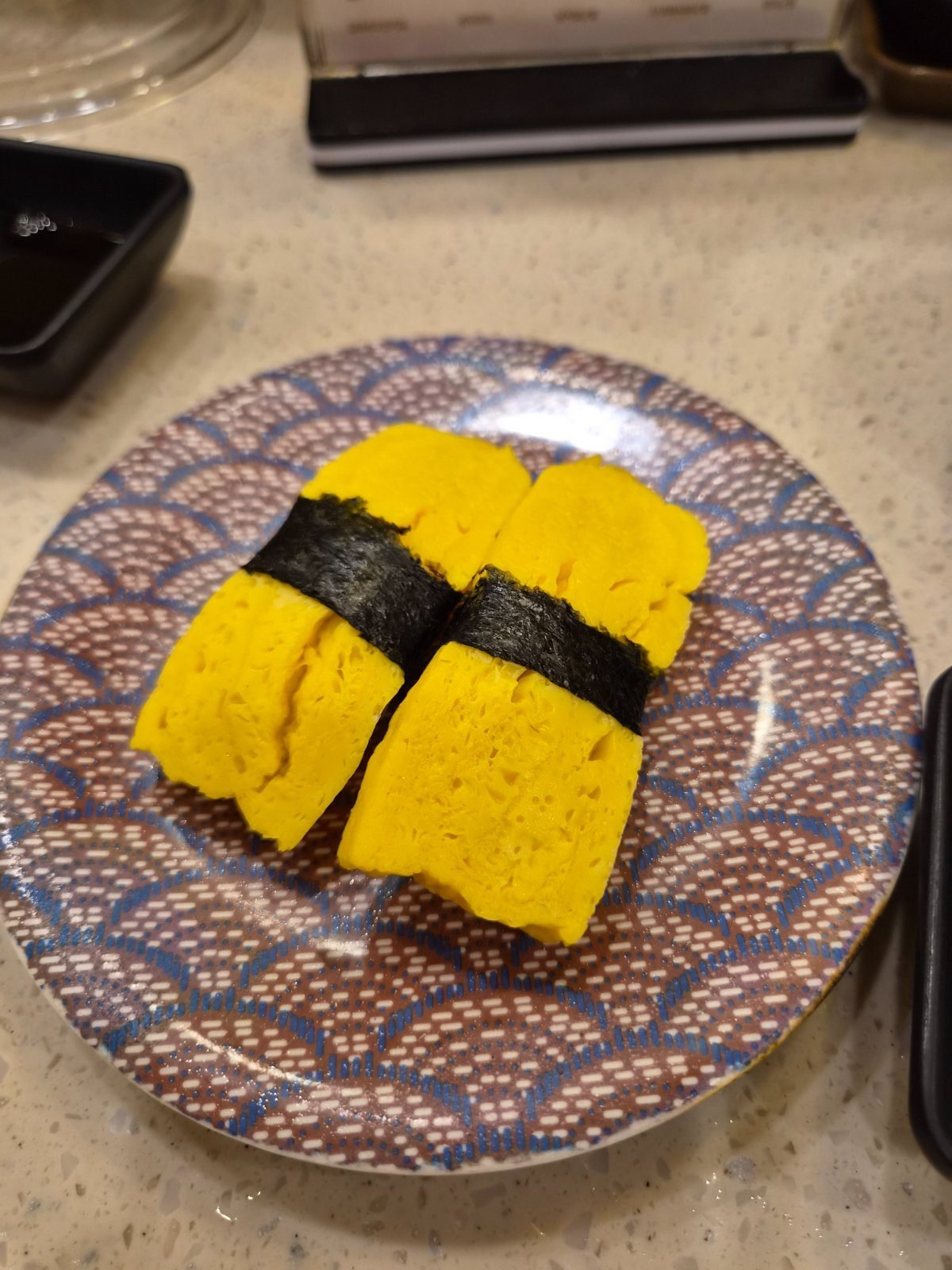 Two pieces of thick Korean-style egg sushi wrapped with a strip of seaweed on a patterned plate