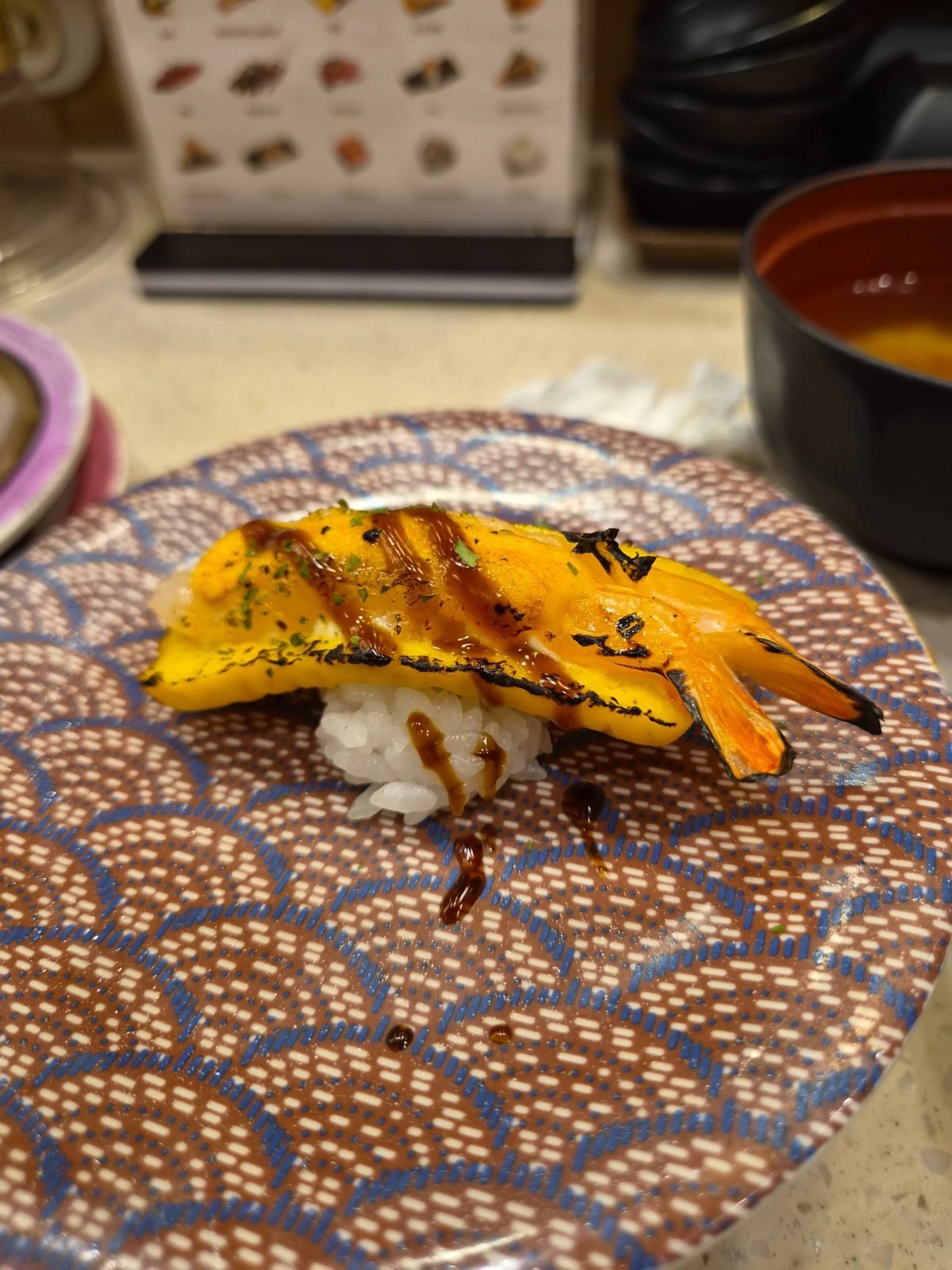 Torched egg and shrimp sushi with browned edges and dark sauce on a patterned plate
