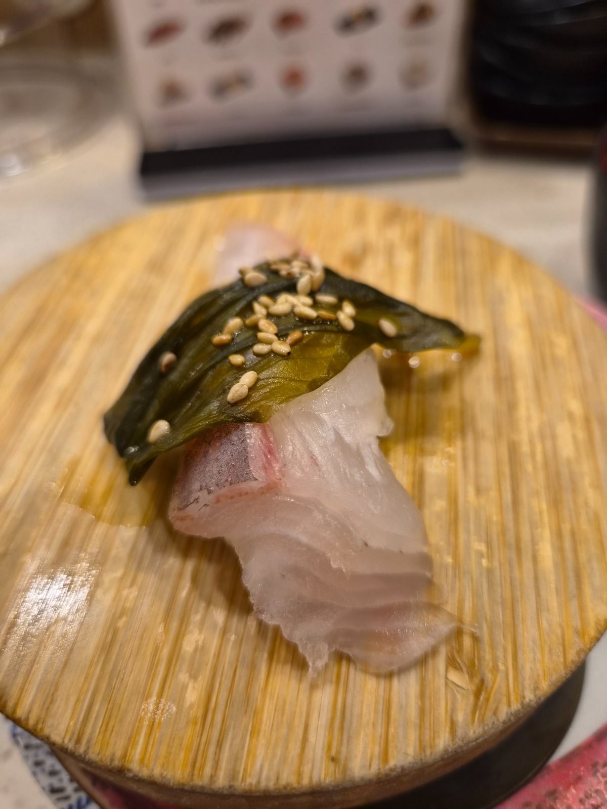 White fish nigiri topped with a dark sheet of seasoned kelp and sesame seeds on a wooden plate