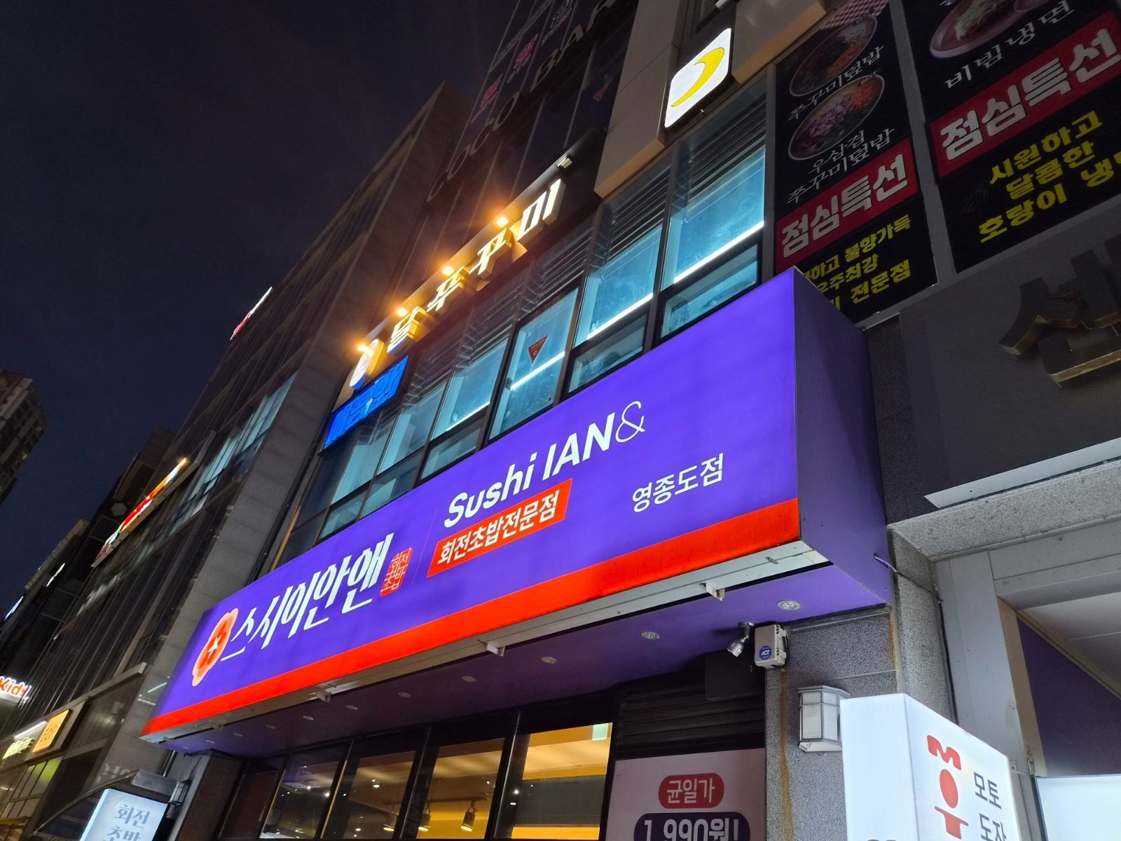 Purple and orange sign reading Sushi IAN& and 스시이안앤 영종도점 above the restaurant entrance at night