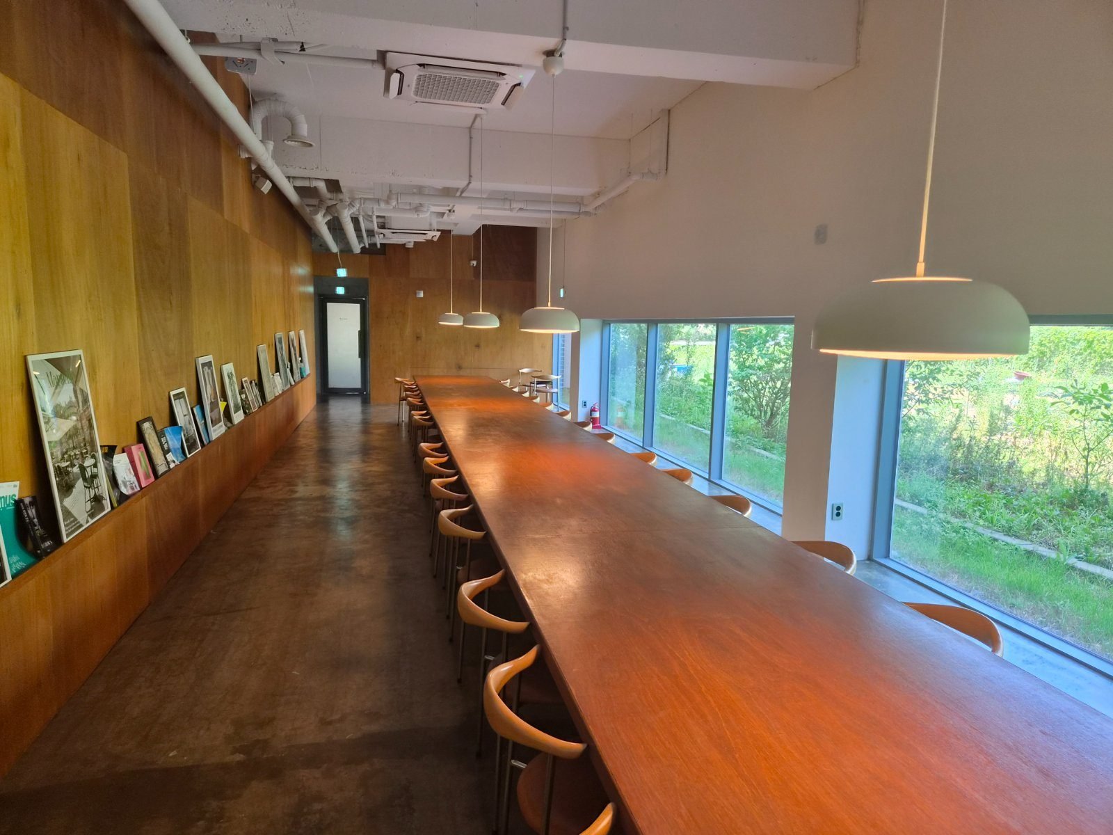 Long wooden communal table along a window with photos and posters on the wall shelf