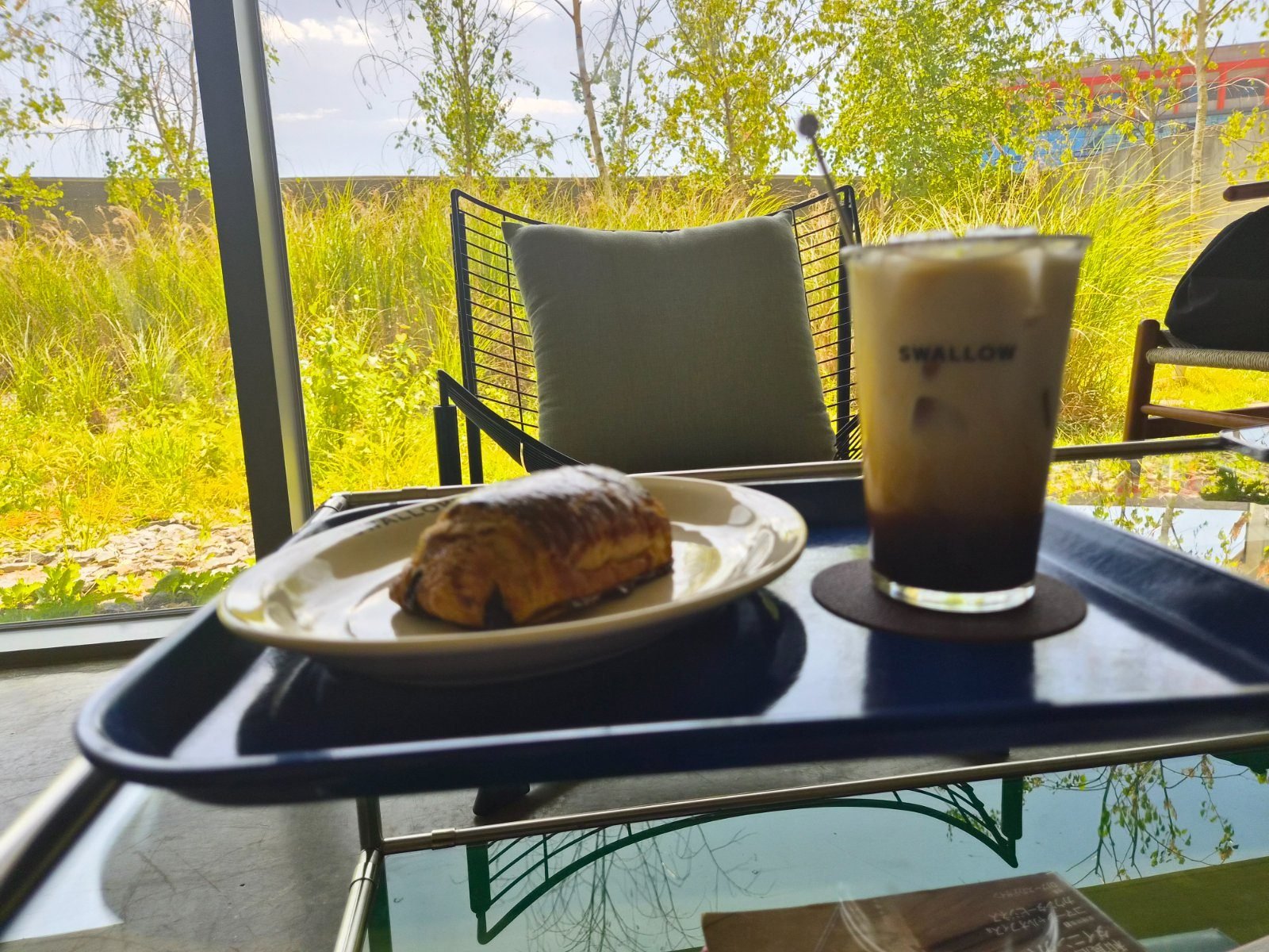 Pain au chocolat on a plate beside an iced americano in a Swallow branded cup on a tray