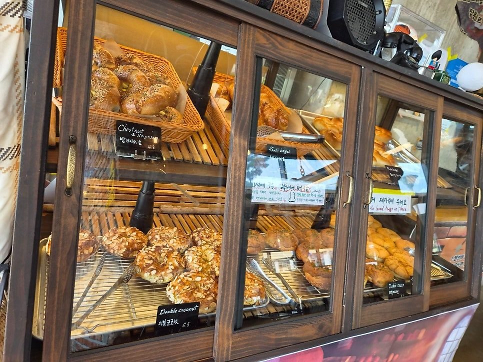 Wooden display case of bagels with chalkboard tags reading Chestnut and Kaya jam 4.2, Double coconut 6.5, Salt bagel and Double onion