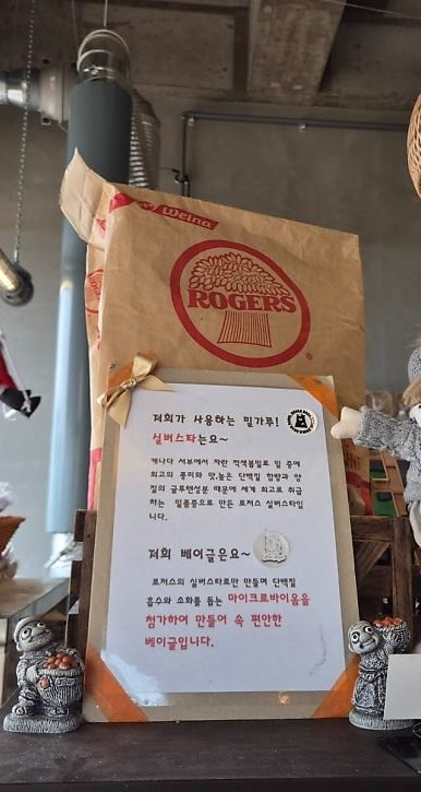 Paper sack of ROGERS flour on a shelf above a Korean notice explaining the bakery uses Rogers Silverstar flour
